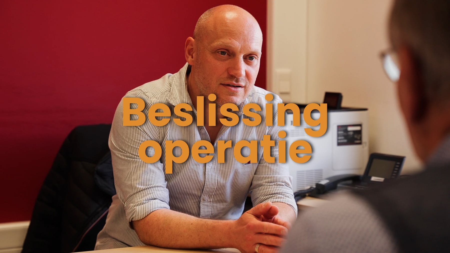 Twee mannen in gesprek aan een bureau, met de titel «Beslissing operatie» in beeld