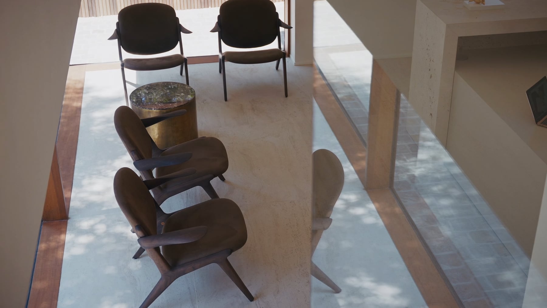 De wachtruimte van de praktijk, met fauteuils, twee stoelen en een ronde bijzettafel in daglicht