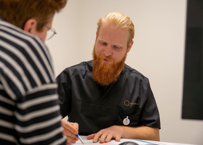 Arts van Orthoca aan zijn bureau, in gesprek met iemand aan de overkant van de tafel