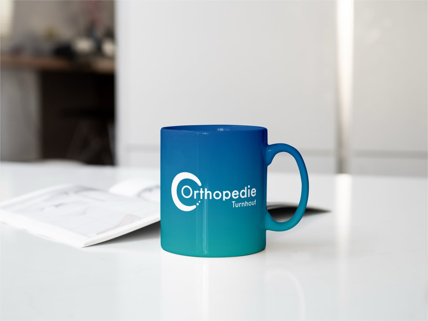 Een mok met het logo van Orthopedie Turnhout naast een notitieblok