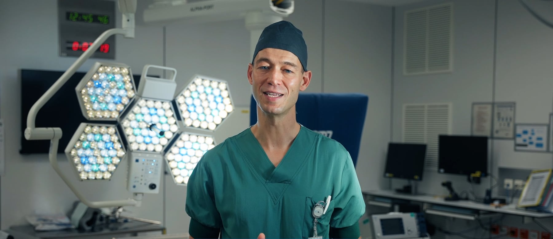 Een chirurg in groene operatiekledij in het operatiekwartier, met de operatielampen achter hem
