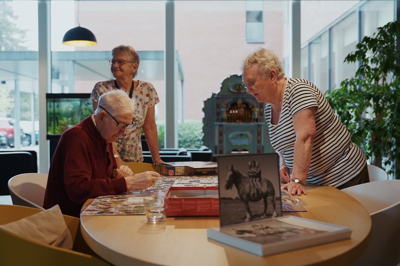 Drie mensen aan een tafel in het woonzorgcentrum, met een oude foto en een boek voor hen